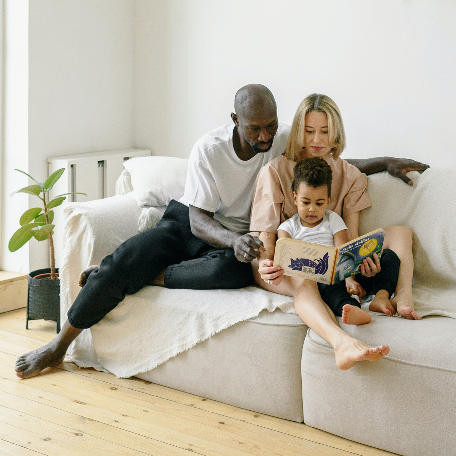 Mother, father and child sharing a book on a sofa